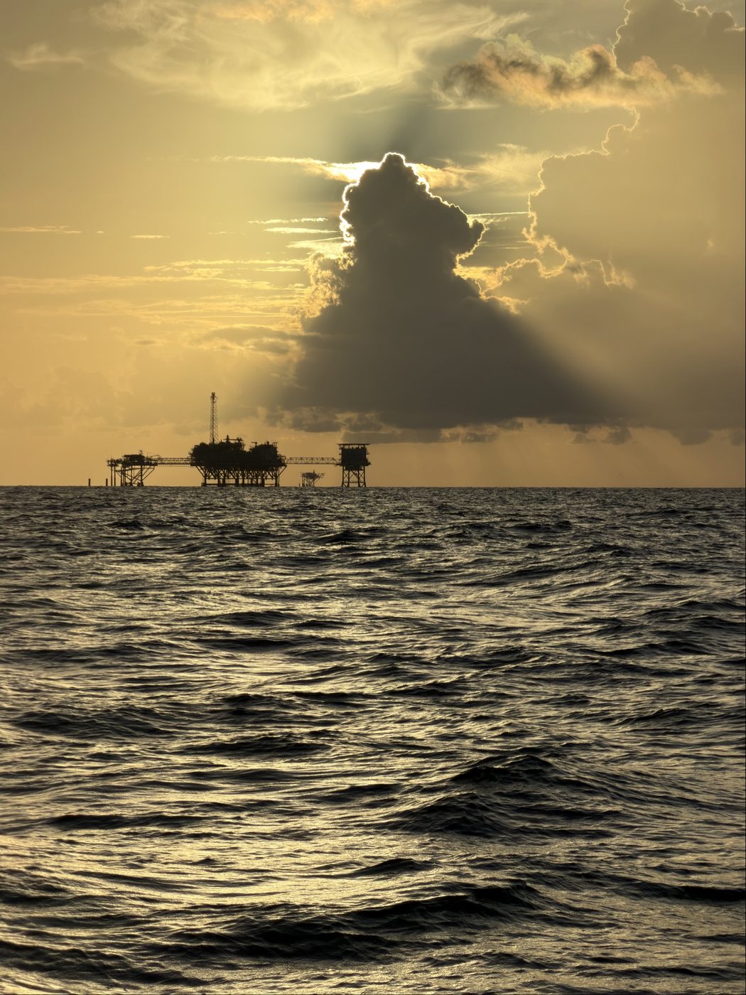 Sunset rays breaking through storm clouds over an offshore rig in the Gulf